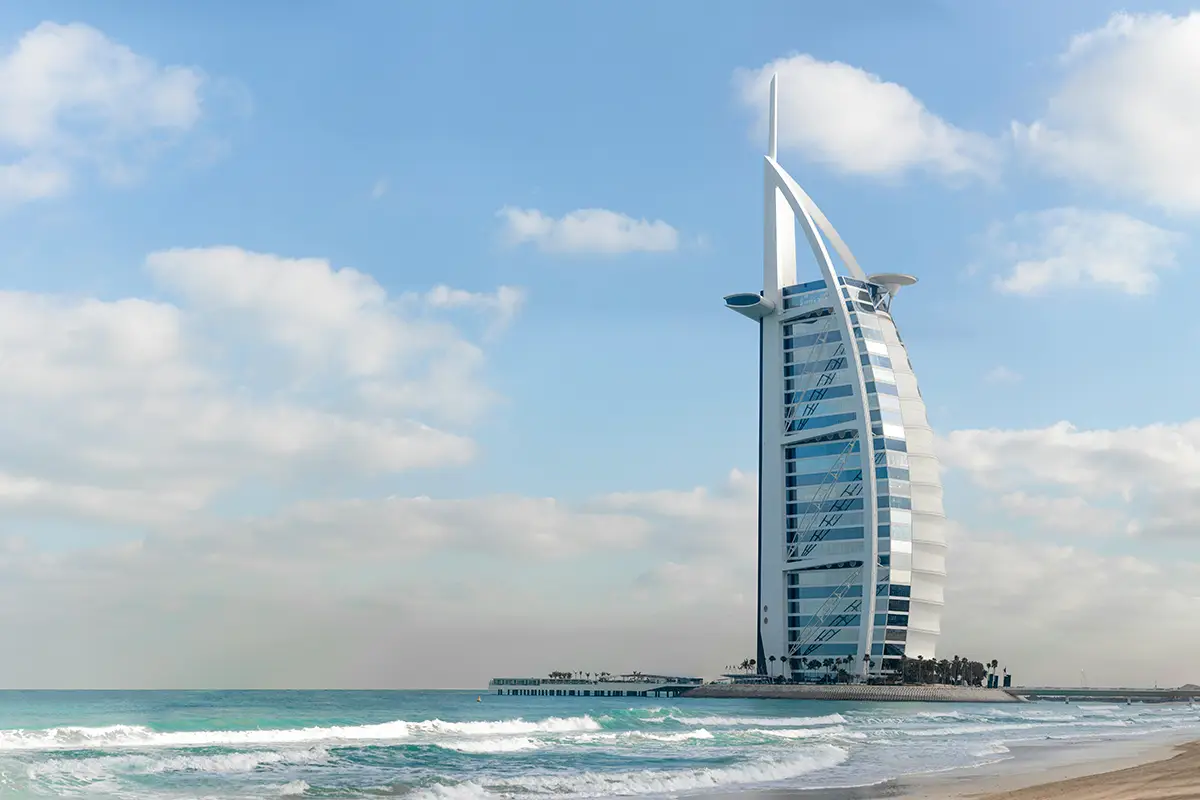 Burj Al Arab hotel by the beach with waves and a clear sky.